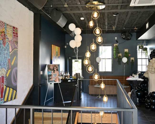 The image shows an interior view of a trendy restaurant or lounge with stylish lighting, modern decor, and a mix of seating areas.