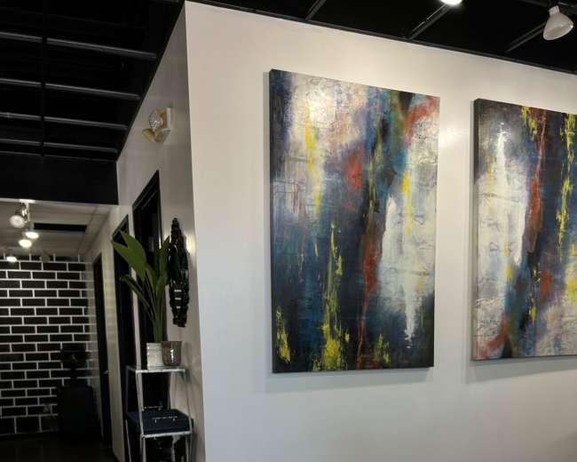 A modern interior space featuring two large abstract paintings on a white wall, a potted plant in a corner, and a black and white brick wall in the background.