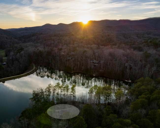 A serene landscape with a lake reflecting trees and a sunset, surrounded by rolling hills.