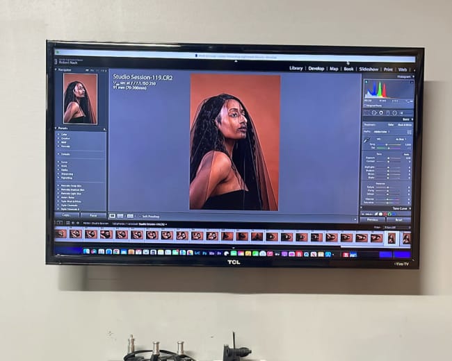 A digital photo is displayed on a monitor, showcasing a model with long hair styled in braids, with various editing tools visible beneath the image.