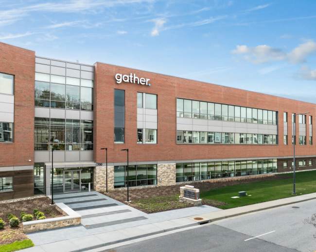 A modern brick building with large windows features the word "gather" prominently displayed on the facade.
