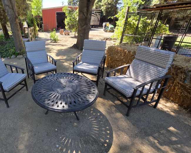 The image shows five outdoor chairs arranged around a circular metal table in a garden setting.