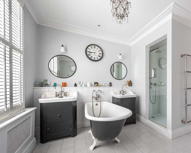 A modern bathroom featuring a freestanding bathtub, two sinks with mirrors above them, a glass shower enclosure, and a view into a living area beyond.