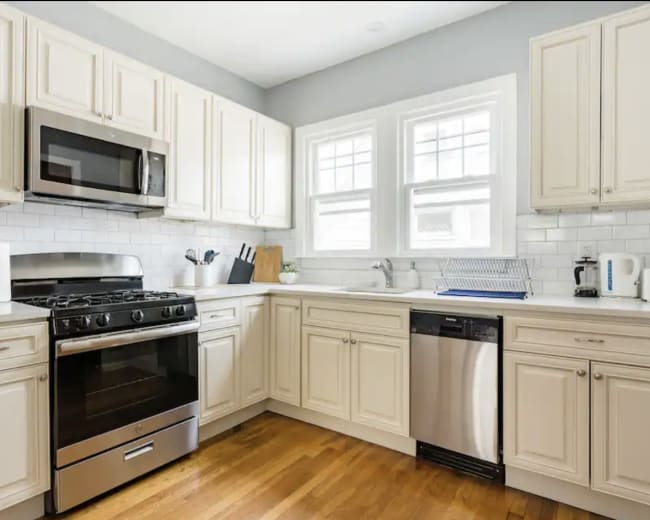 A modern kitchen features white cabinetry, stainless steel appliances, and a hardwood floor.
