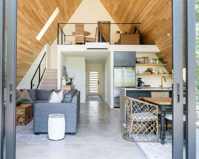 A modern, open-concept living space with high wooden ceilings, a kitchen area, a dining table, and a cozy seating area.