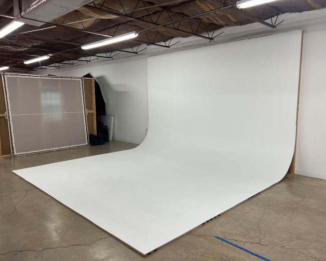 A spacious photography studio with a large, seamless white backdrop and polished concrete floors.