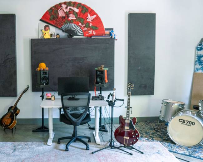 The image shows a_music studio featuring a desk with a chair, various musical instruments, a large blackboard, and decorative wall elements.