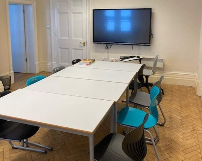 A modern conference room features a large table surrounded by colorful chairs and a wall-mounted television.