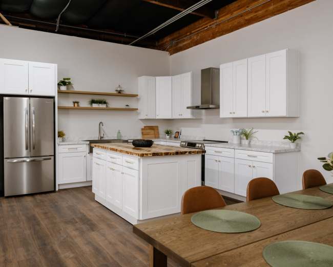 A modern kitchen features white cabinetry, a marble countertop, stainless steel appliances, and a dining table set with green place mats.