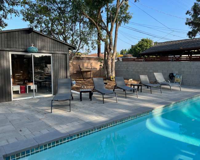 A backyard with a swimming pool, several lounge chairs arranged by the poolside, and a small shed in the background.