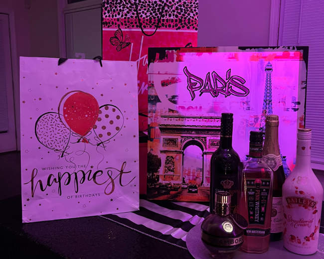 A collection of colorful birthday gift bags and a display of various liquor bottles on a black table.