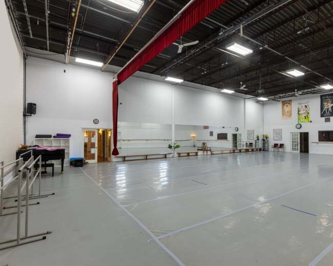 The image shows a spacious dance studio with a shiny floor, mirrors along one wall, and various artworks and decorations hanging on the other walls.