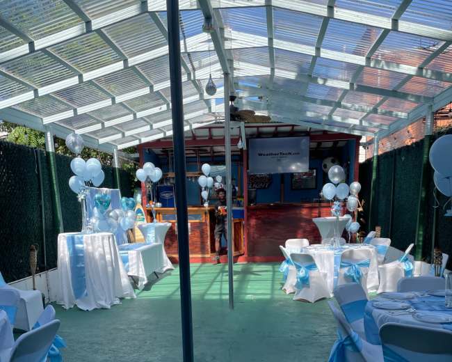 A decorated outdoor space with tables set up for a celebration, featuring blue and white balloons and table linens.