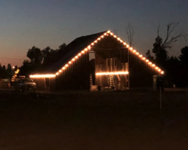 A barn is outlined with string lights against a twilight sky.