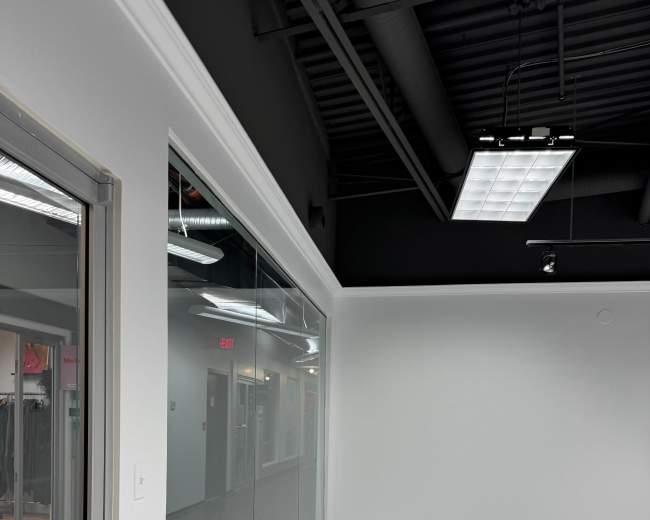 The image shows a spacious, empty room with a large glass window on one wall and a doorway leading to another area.