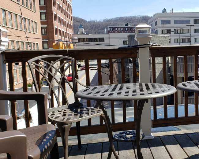 A wooden deck with two round metal tables and four chairs overlooking a city street and buildings in the background.