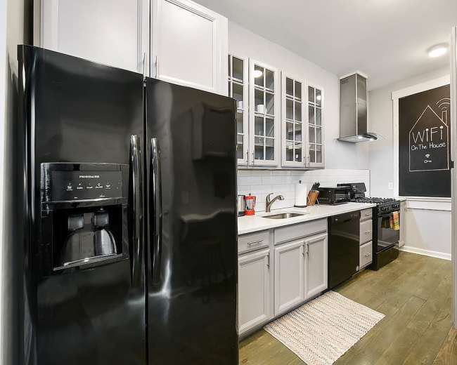 A modern kitchen features black appliances, white cabinetry, and a chalkboard wall listing WiFi details.