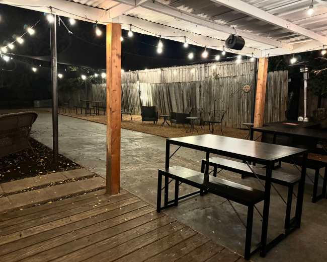 A patio area features a picnic table and benches, string lights overhead, and a concrete floor surrounded by wooden fences.