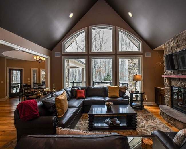 A modern living room features large arched windows, a stone fireplace, and a dark leather seating arrangement with a coffee table.