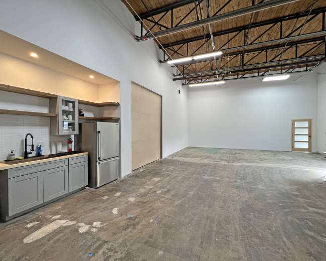 The image shows an empty industrial space with a kitchenette on one side and smooth concrete flooring.