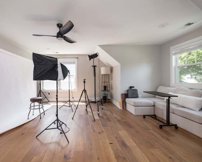 A photography studio setup includes a white backdrop, lighting equipment, and a seating area with a small table.