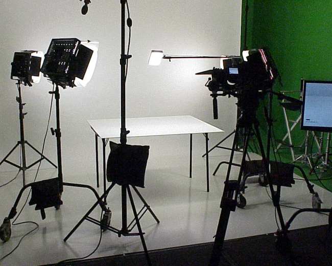 A photography studio is set up with cameras and lights positioned around a white table against a green backdrop.