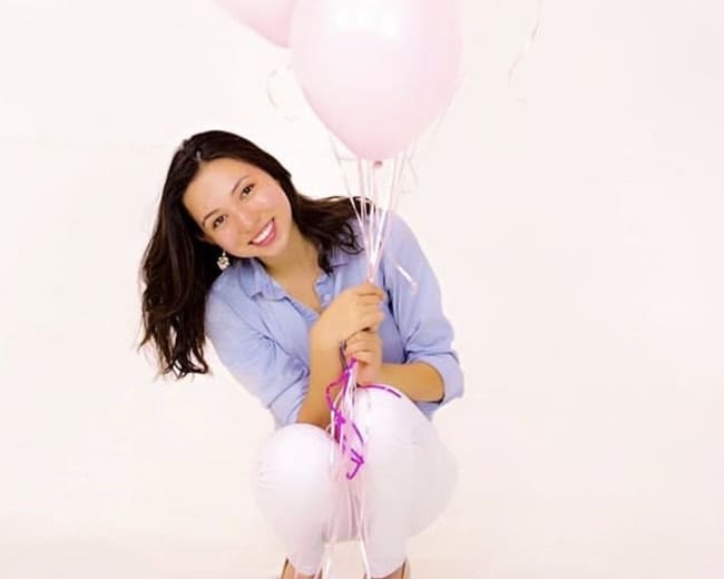 A person kneels while holding a bouquet of pink balloons against a white background.