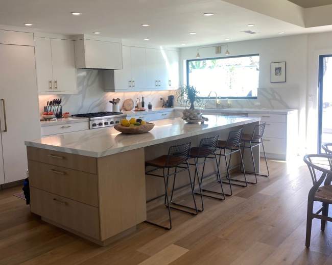 A modern kitchen with white cabinetry, a central island with seating, and large windows that allow natural light in.