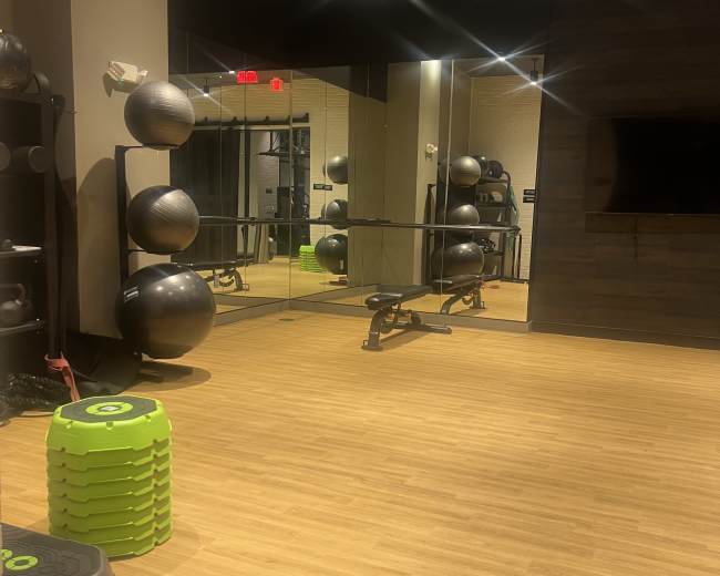 The image shows a fitness studio featuring exercise equipment, a large mirror, and a wooden floor.