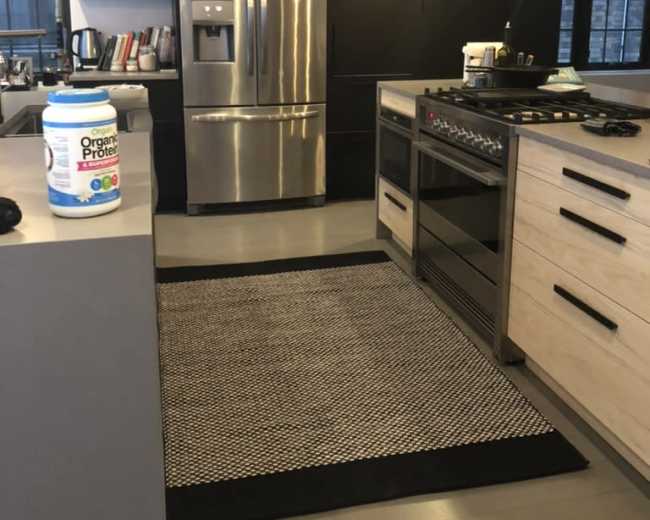 The image shows a modern kitchen featuring a stainless steel refrigerator, a gas stove, and a central island with a black and white rug.