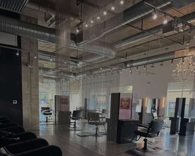The image shows a modern hair salon with styling stations, salon chairs, and a row of shampoo bowls under soft lighting.