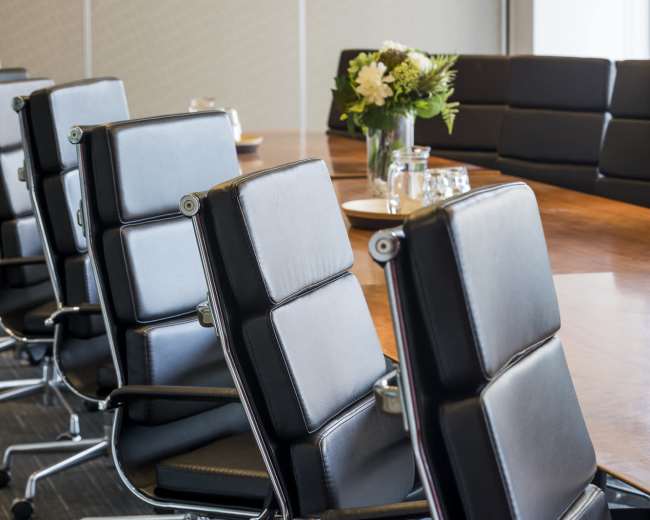 The image shows a conference room with a long wooden table surrounded by black office chairs.