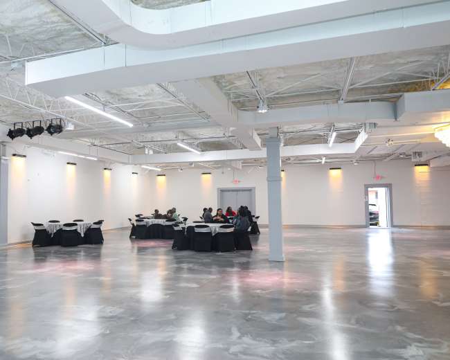 A spacious, modern event hall with gray flooring and tables set for a gathering.