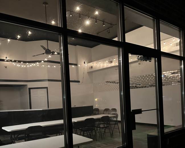 The image shows a dimly lit interior of a venue featuring several tables and chairs arranged for an event.