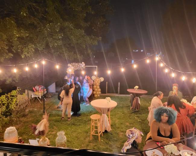 A garden party is illuminated by string lights, featuring guests dancing and dining among decorated tables.