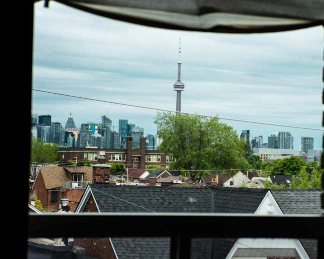 The view from the window frames a skyline with the CN Tower prominently rising above a collection of rooftops and greenery.