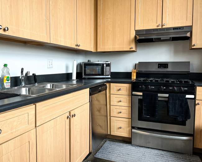 The kitchen features wooden cabinets, a black countertop, a sink, a stainless steel gas stove, a microwave, and a dishwasher.