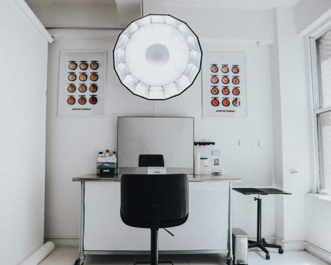 A minimalist room features a central table with a chair, an overhead light, and color palettes mounted on the wall.