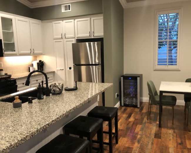 A modern kitchen with white cabinetry, stainless steel appliances, a granite countertop, and a dining table with green chairs.