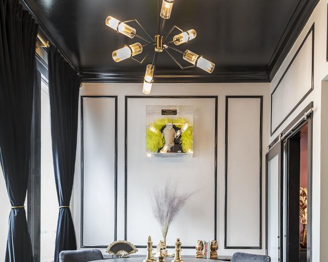 A dimly lit dining area featuring a round black table surrounded by two upholstered chairs, adorned with decorative objects on the table and framed artwork on the wall.