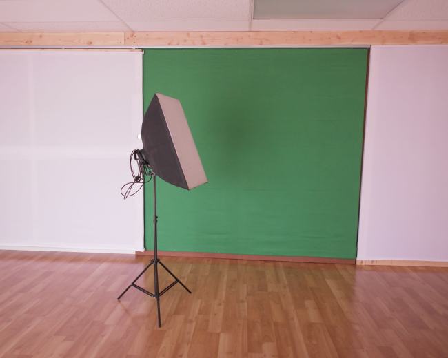 The image shows a studio space with a green backdrop and a lighting setup on a stand.