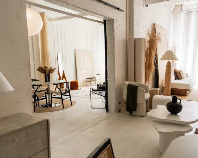 The image shows a modern, minimalist interior space featuring various pieces of furniture, including lamps, a sofa, and decorative items, all arranged in a well-lit area with large windows.