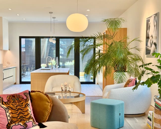 A modern living space features a large window with views of an outdoor area, complemented by stylish furniture, plants, and decorative elements.