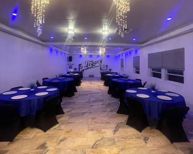 The image shows a banquet hall with round tables covered in blue tablecloths, black chair covers, and sparkling chandeliers, illuminated with blue lighting.