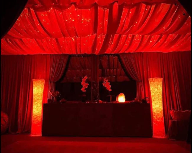 The scene features a room with red draped curtains, illuminated by glowing red lamps on either side of a central counter.