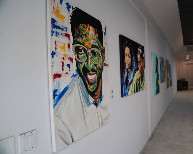 The image shows a gallery hallway featuring a series of colorful portraits displayed on the walls.