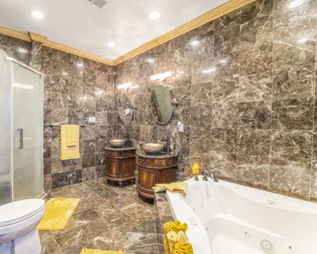 The bathroom features marble walls, two circular mirrors above wooden vanities with vessel sinks, a glass shower, and a jetted bathtub.
