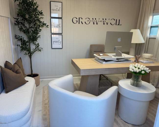 The image shows a modern office space featuring a wooden desk with a computer, a cozy seating area with two armchairs, and decorative wall art.