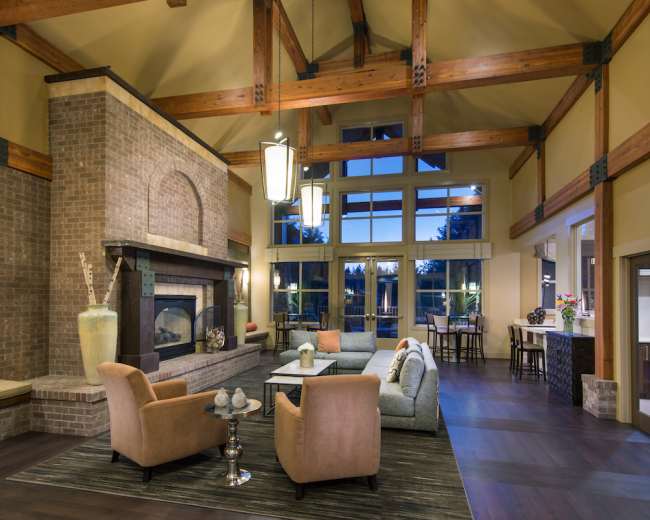 A spacious, well-lit lounge area featuring high wooden beams, a brick fireplace, and comfortable seating arrangements.