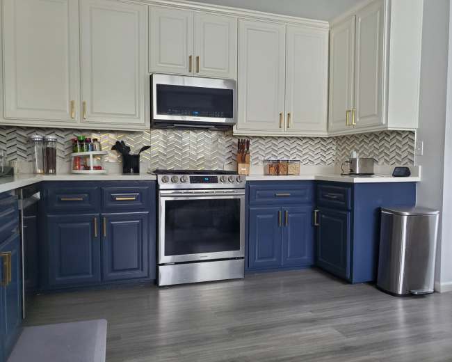 The image shows a modern kitchen featuring blue cabinets, stainless steel appliances, and a herringbone-patterned backsplash.